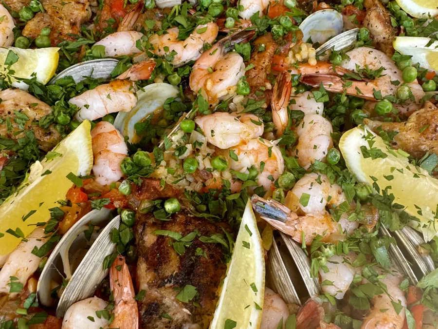 A wide pan of seafood paella with shrimp, clams and lemon